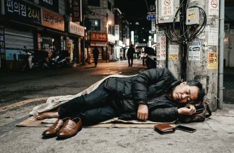 50대 남성이 술에 취해 길거리 모퉁이 전봇대 옆에서 신발을 벗고 머리근처에 지갑을 두고 잠들어 있다.